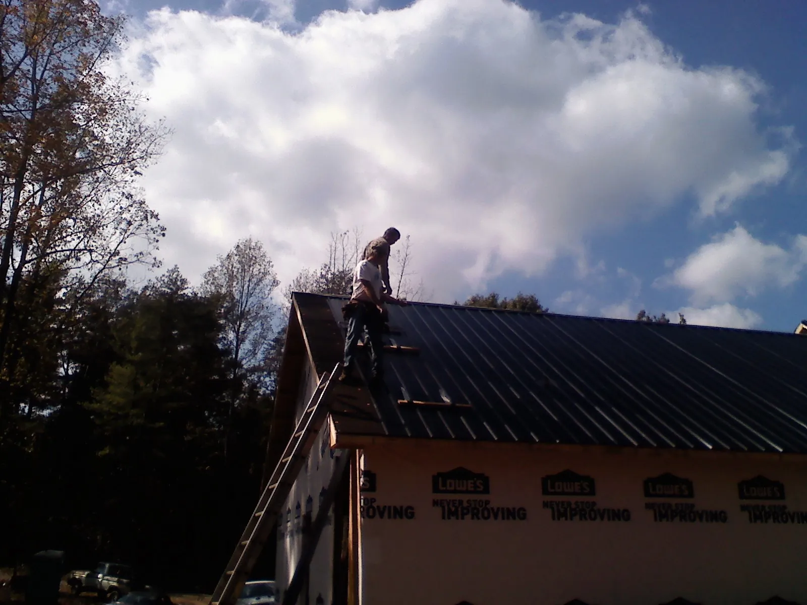 Roofer fastening dark metal panels high against a cloudy sky, from a Roof Inspection job in Twin Lakes