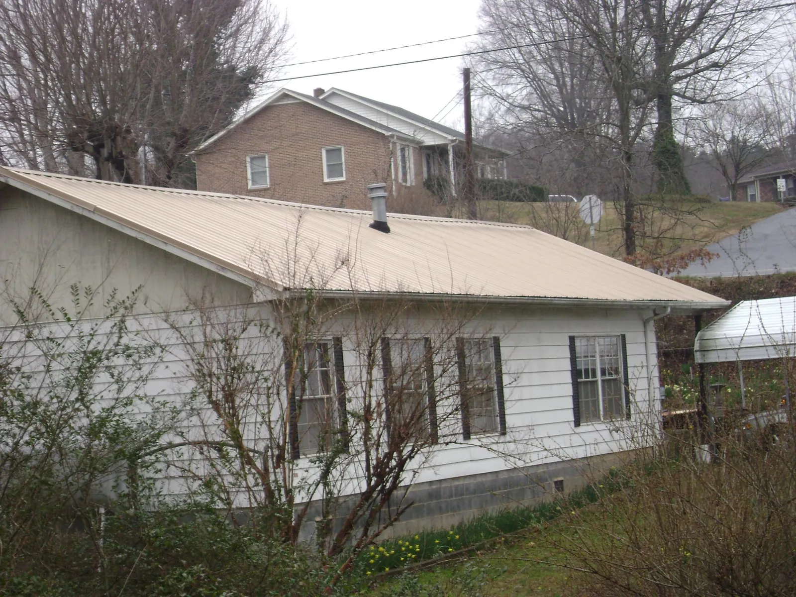 Tan metal roof on a white sided house set into a hillside — Commercial Roofing by Roofing Brothers in Twin Lakes